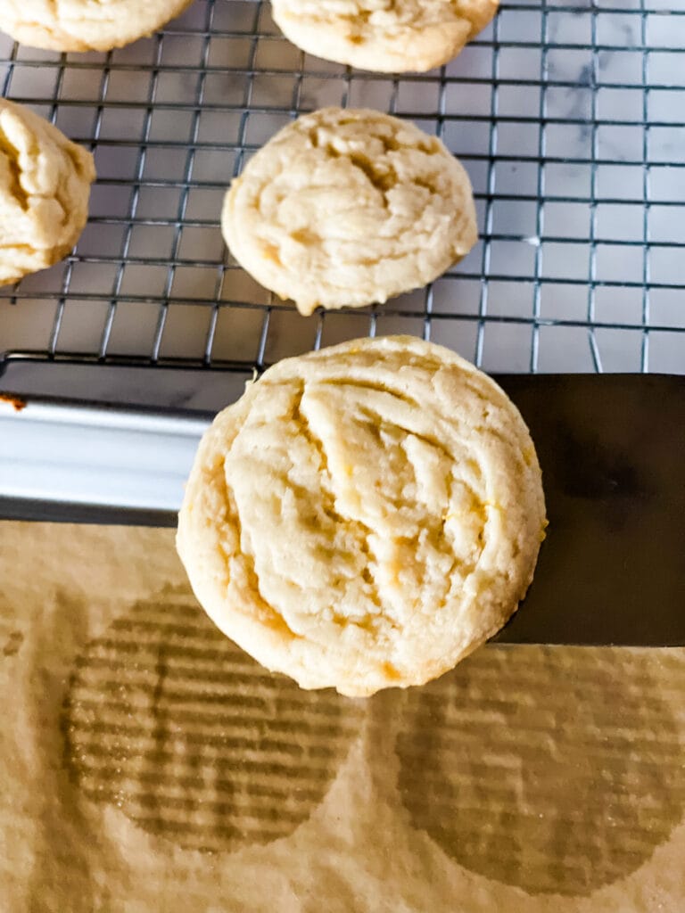 Removing a baked lemon cookie with a spatula onto a wire cooing rack with the other baked cooling cookies.