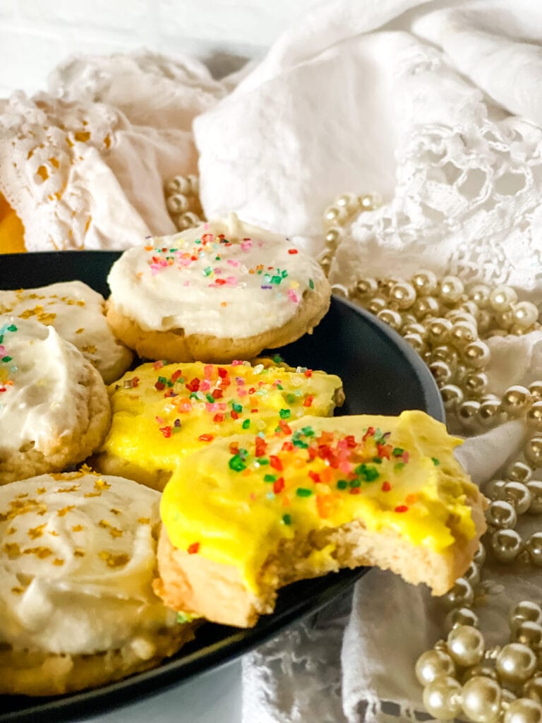 Plate of vegan lemon sugar cookies - some with white frosting and some with yellow and all with sprinkles on a black plate.
