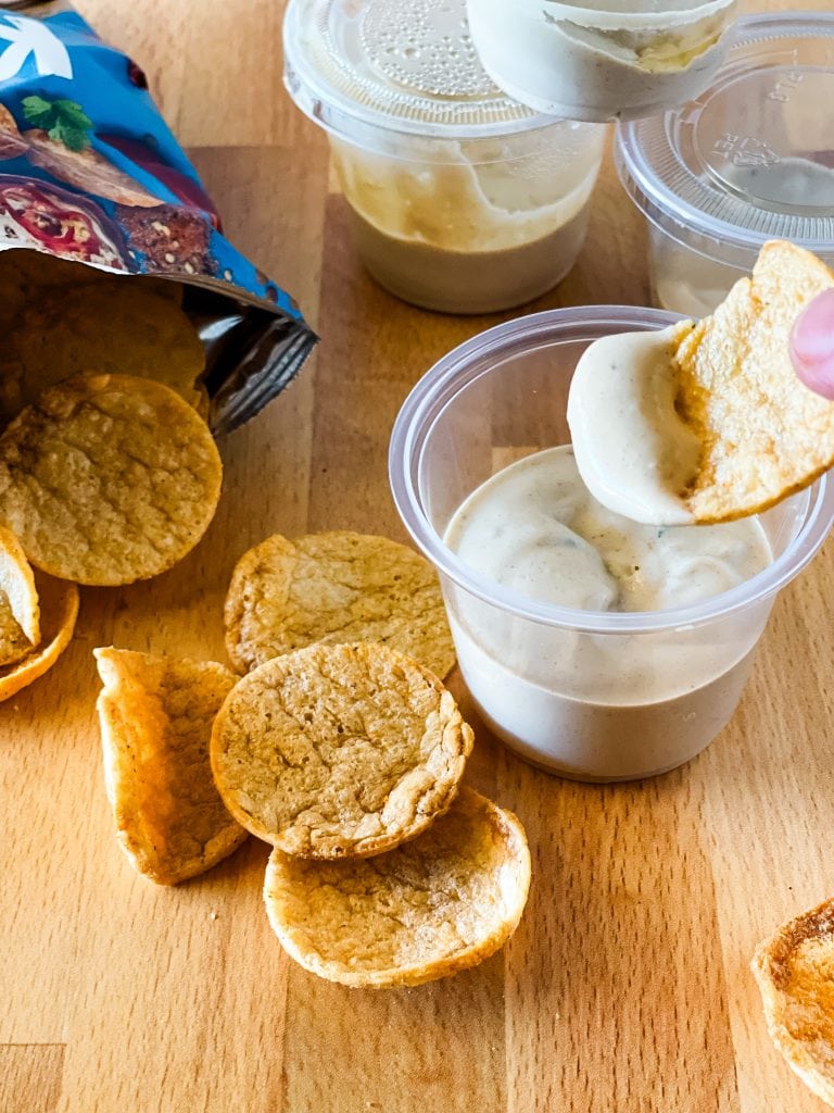 A small cup with a portion of tofu dip. A chip is dipping out a small amount of dip.