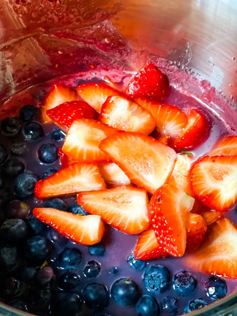 The blueberries and cut strawberries in the sieved raspberry jam mixture.