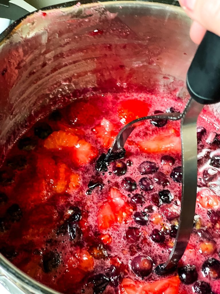 Mashing the cooked berries with a potato masher.