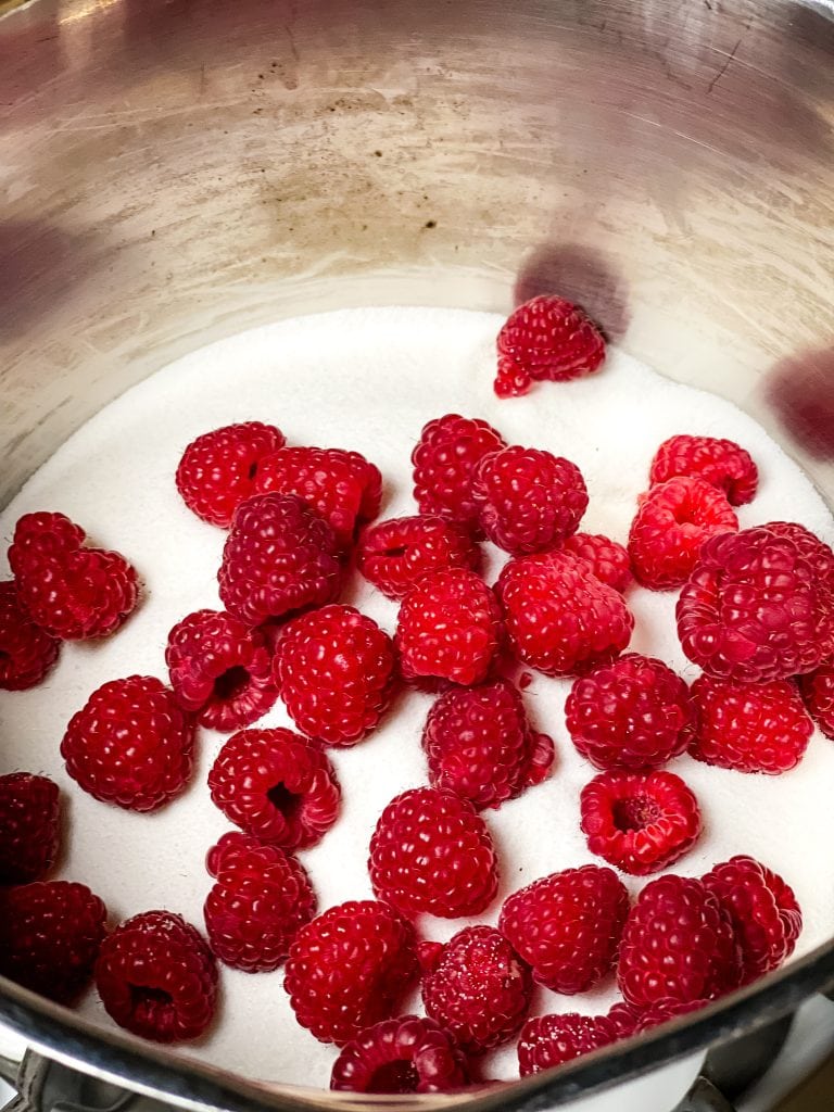 Whole raspberries on top of granulated sugar in a sauce pan.