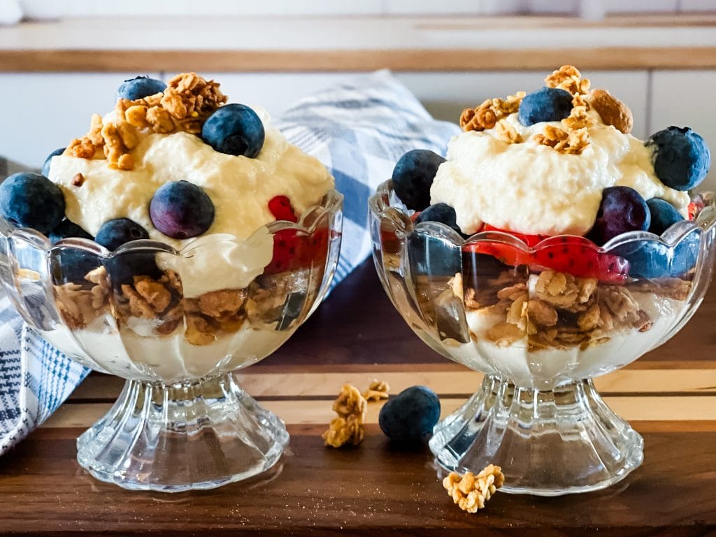 Two glass bowls of vegan greek yogurt topped with blueberries, strawberries, and granola.