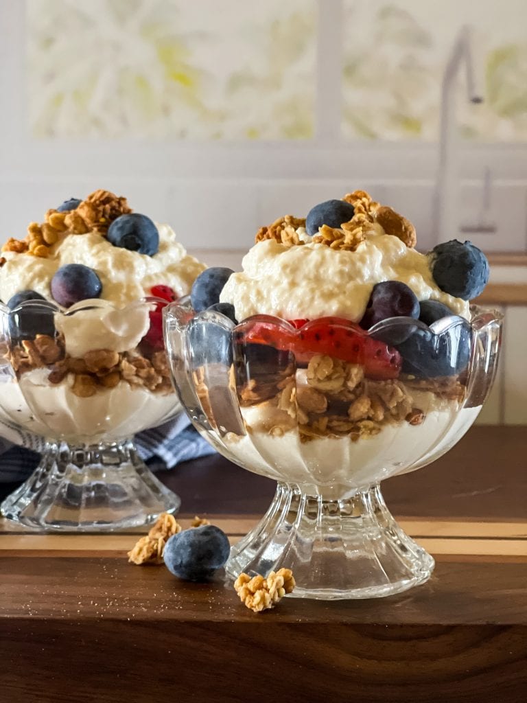 Two glass bowls of vegan greek yogurt topped with blueberries, strawberries, and granola.