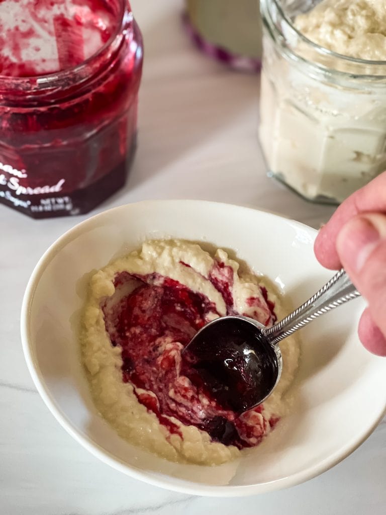 Mixing jam into the greek yogurt. A jar of jam is to the left rear and a jar of yogurt is to the right rear.