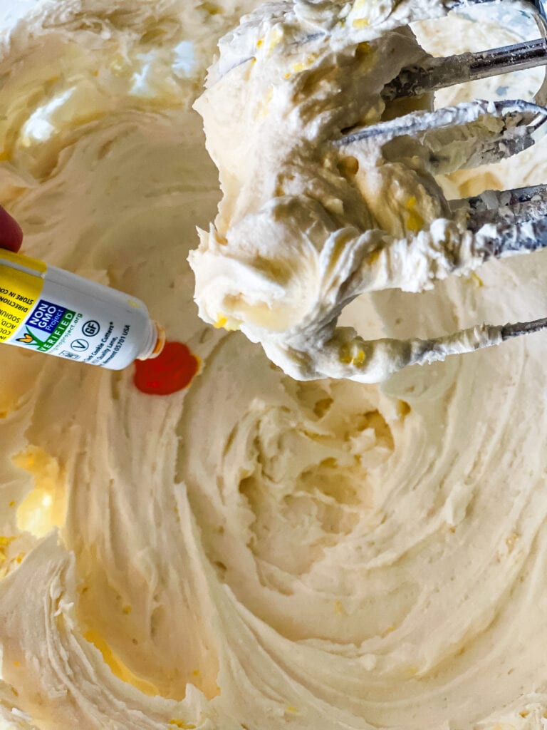 Adding some yellow food coloring gel to the lemon frosting. The beaters are lifted from the bowl.
