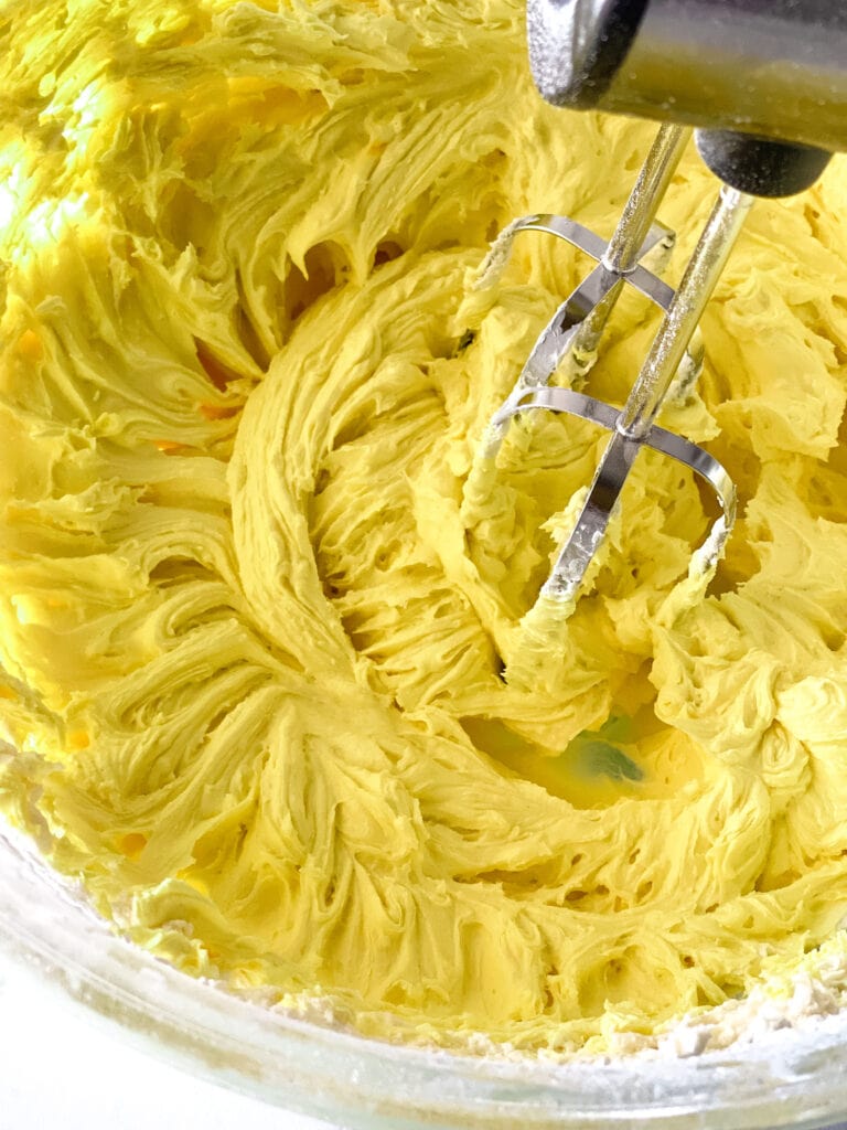 Beaters in the bowl of lemon frosting. The frosting is yellow because it's been colored with yellow food coloring.