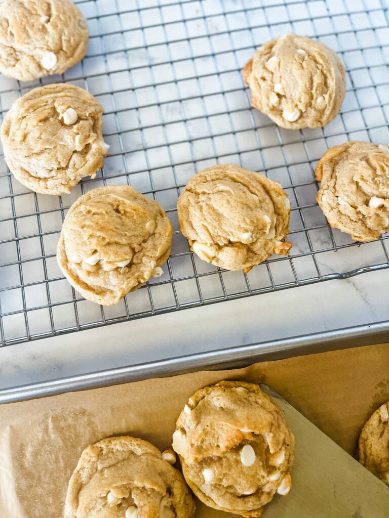 A cooling rack with white chocolate macadamia nut cookies with a few in front on a parchment paper.