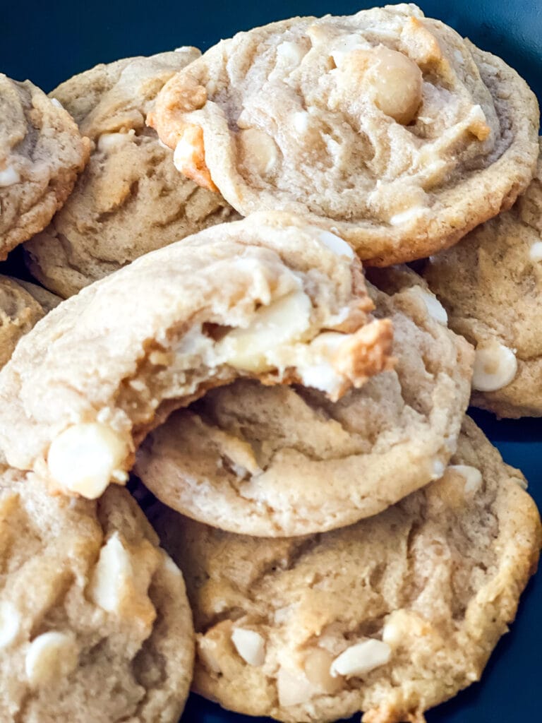 Pile of vegan white chocolate macadamia nut cookies with one with a bite removed.