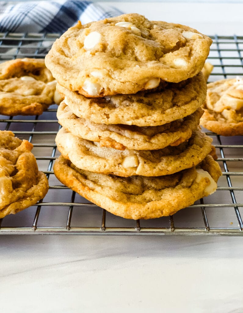 Stack of vegan white chocolate macadamia nut cookies on a wire rack with a gray checked cloth behind.
