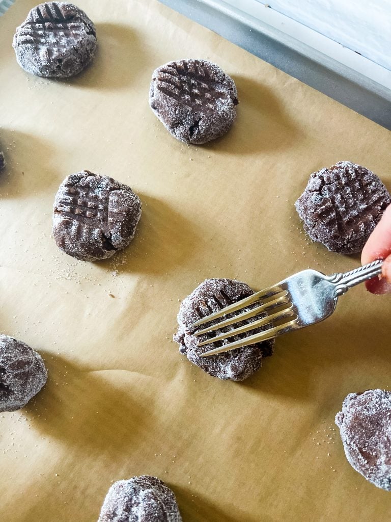 Making hatch marks with a fork on top of unbaked chocolate peanut butter cookies.