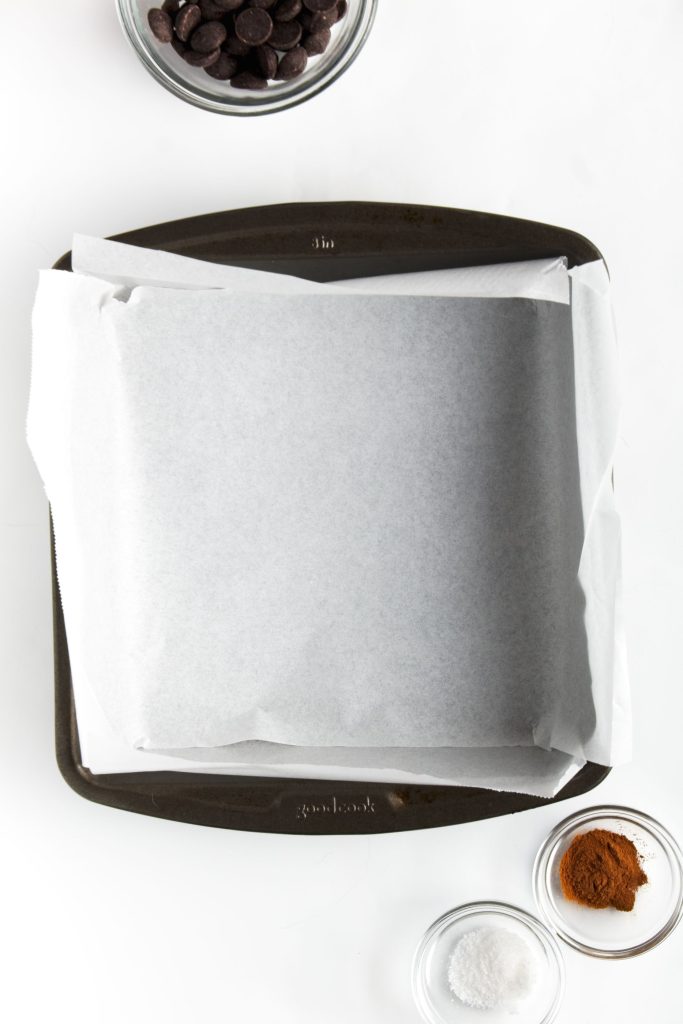 Lining an 8x8 pan with parchment paper showing the criss cross method.