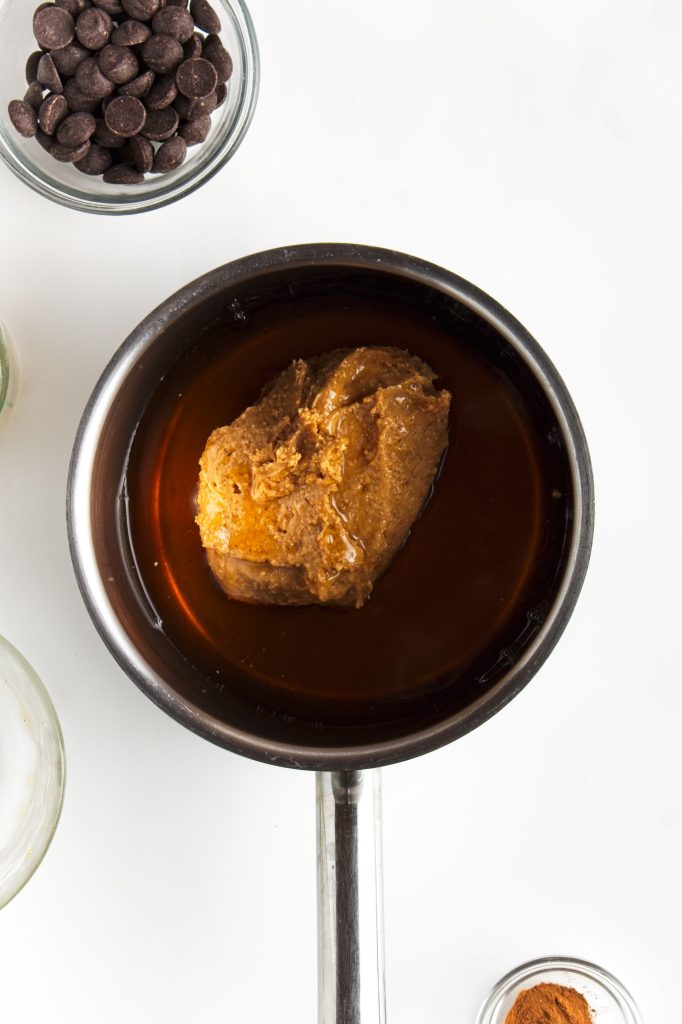Adding the peanut butt4er and maple syrup to the small pan. Bowl of chocolate chips in top left corner.