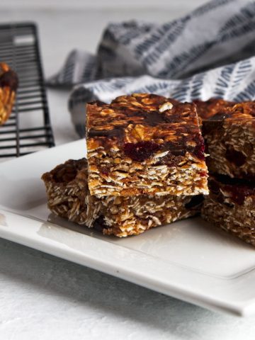the cut peanut butter oat bars on a wire rack in top left corner, and on a white square plate in center with a grey squiggle striped napkin top right.