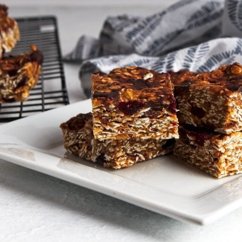 the cut peanut butter oat bars on a wire rack in top left corner, and on a white square plate in center with a grey squiggle striped napkin top right.