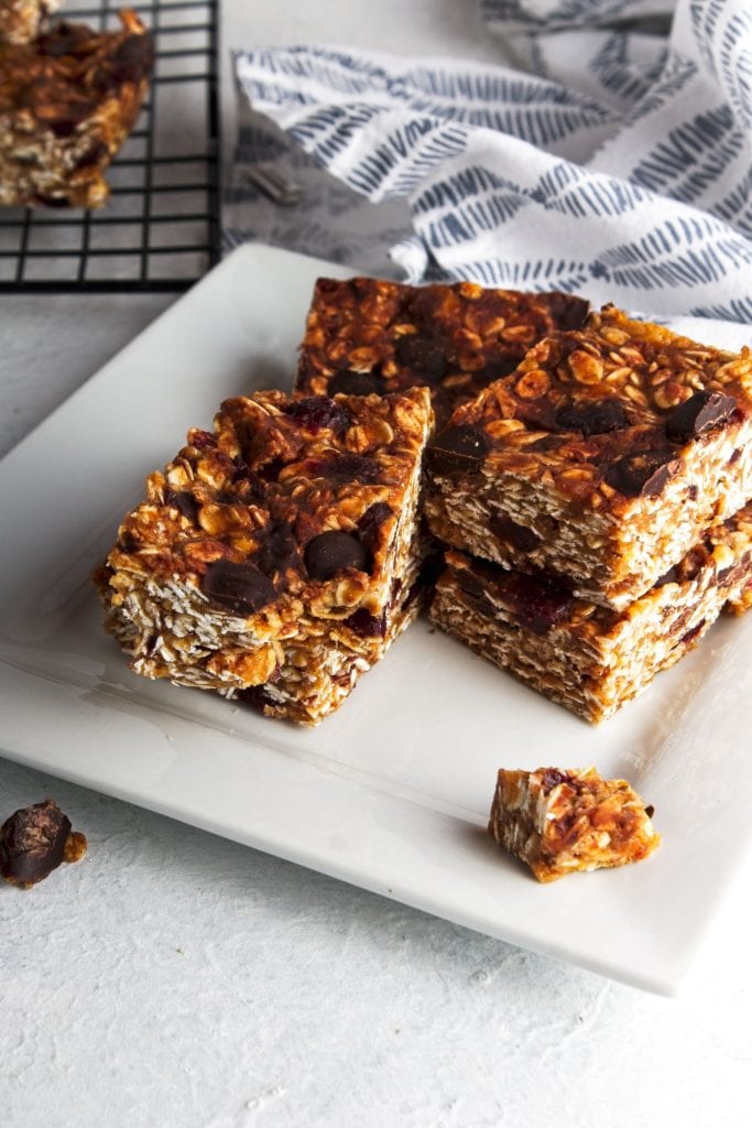 the cut peanut butter oat bars on a wire rack in top left corner, and on a white square plate in center with a grey squiggle striped napkin top right.