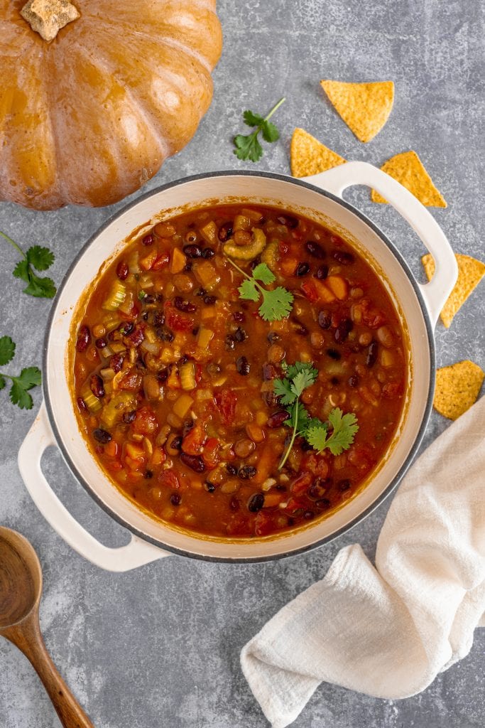 Hearty vegan pumpkin chili with vegetables in a white pot, garnished with cilantro. Perfect healthy veggie recipe for all ages.