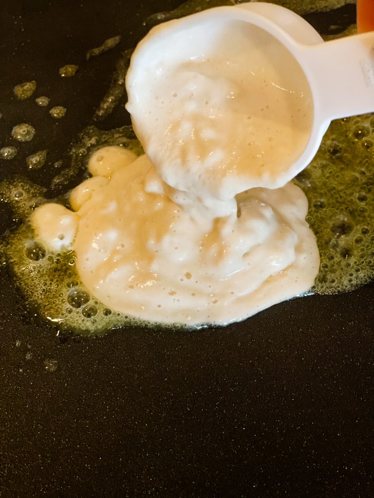 Pouring the batter onto a griddle sizzling with melted vegan butter.