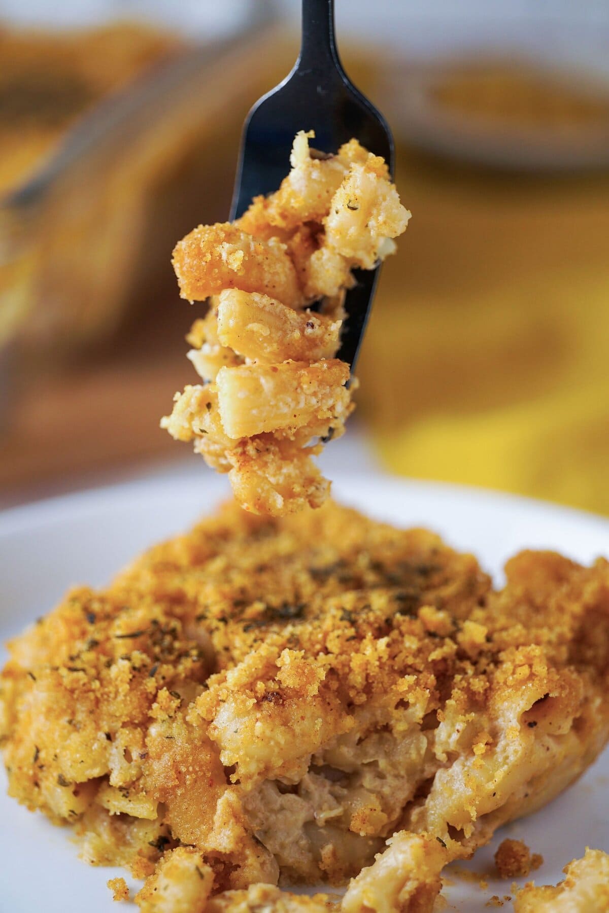 baked mac and cheese on a dish with a black forkful in the air above it