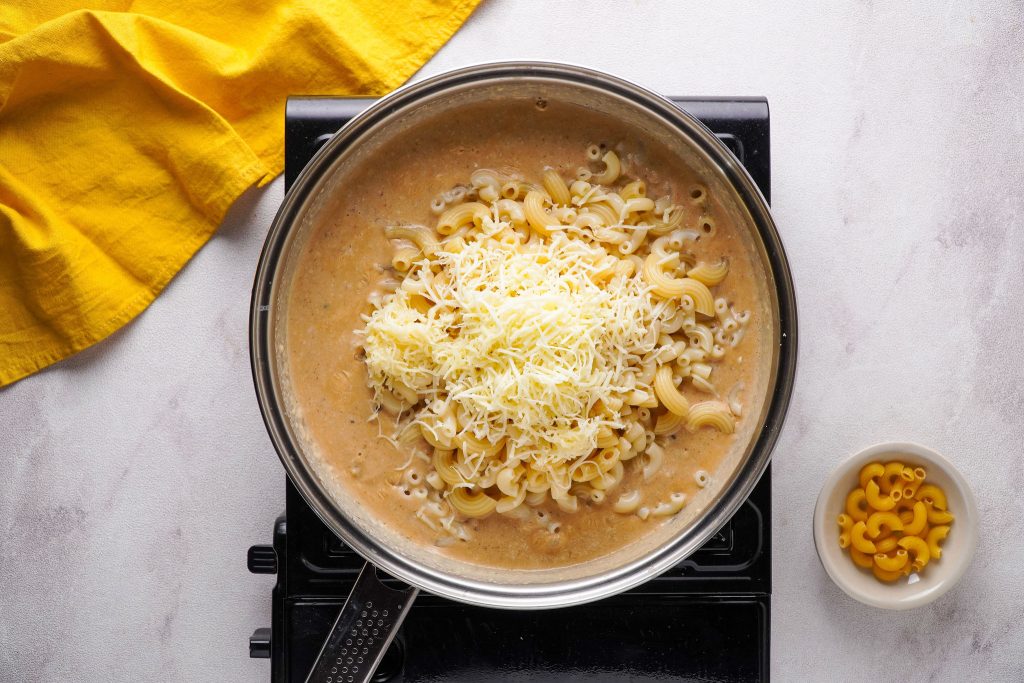 Shredded vegan cheese on top of cooked macaroni in pot on stovetop