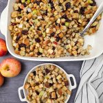 Vegan stuffing with apples and cranberries for healthy eating. In a casserole dish with a large spoon an small rounds dish. Apples on the side.