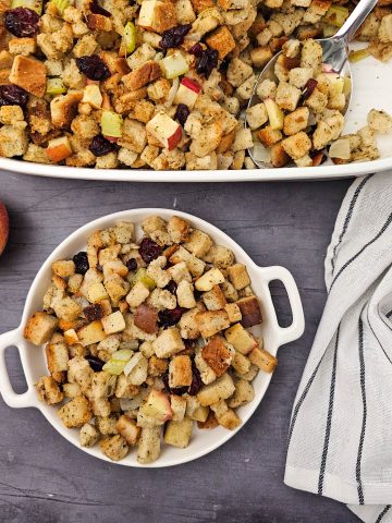 Vegan stuffing with apples and cranberries for healthy eating. In a casserole dish with a large spoon an small rounds dish. Apples on the side.