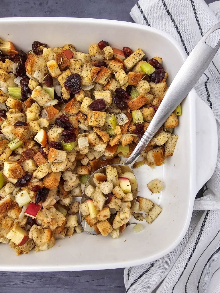 Vegan stuffing with apples and cranberries for healthy eating. In a casserole dish with a large spoon an small rounds dish. Apples on the side.