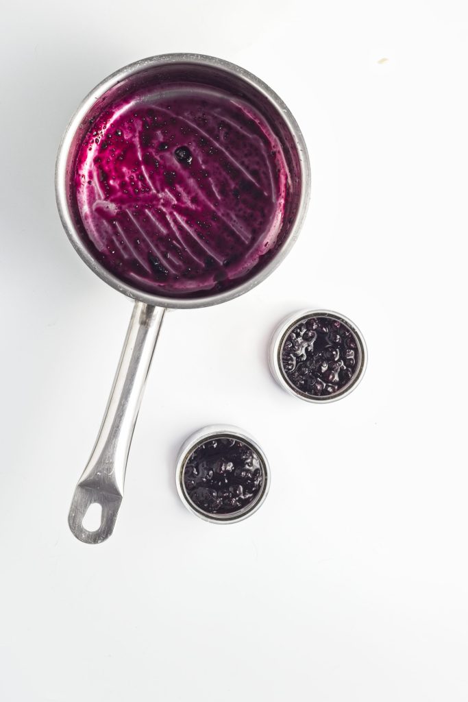 Blueberry compote mixture in bottom of two parfait cups with an empty pan with with blueberry compote mixture top left