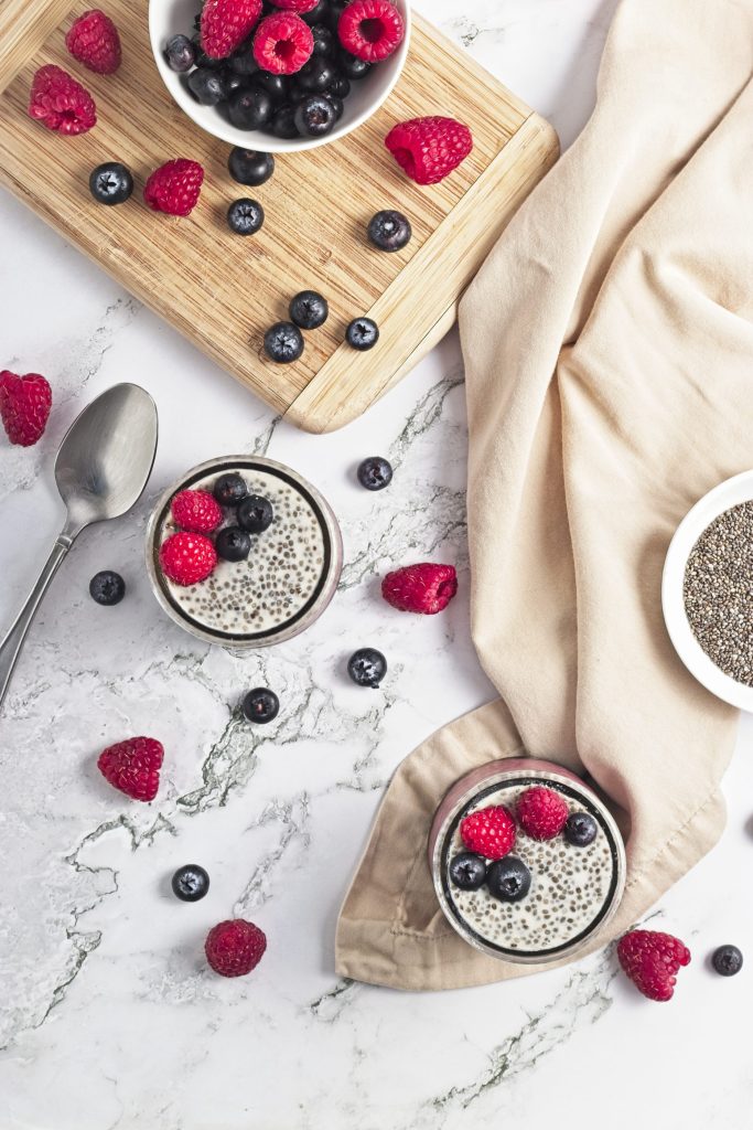 Fresh mixed berries on marble surface and two cups of berry chia pudding promoting healthy vegan snacks from Veggie Fun Kitchen.
