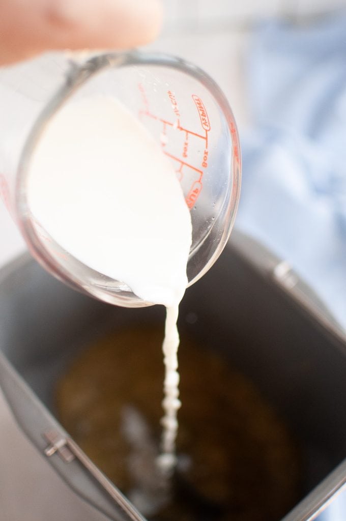 Pouring warmed plant milk in the bread machine pan