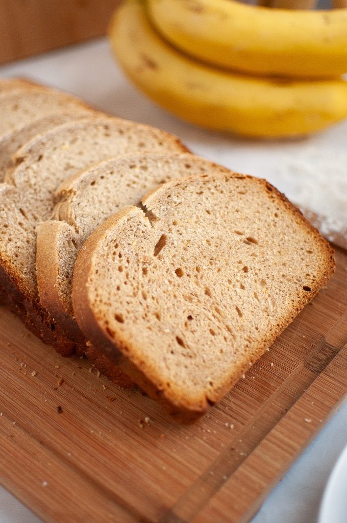 Two slices of homemade banana bread on a white plate, set on a light-colored surface next to a blue cloth and a partially visible banana.