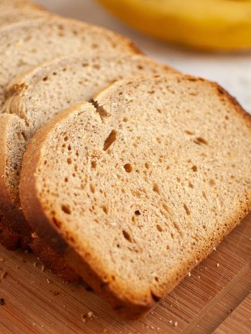 Two slices of homemade banana bread on a white plate, set on a light-colored surface next to a blue cloth and a partially visible banana.