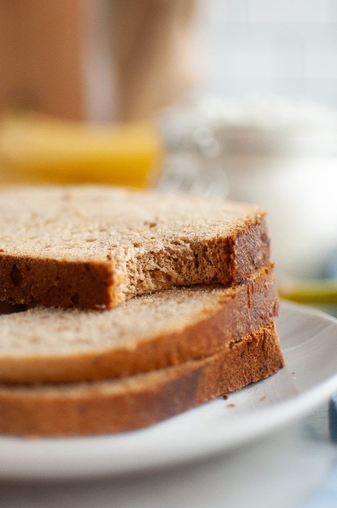 Two slices of yeasted banana bread stacked on a white plate, with a bite taken out of the top slice. The background is softly blurred.