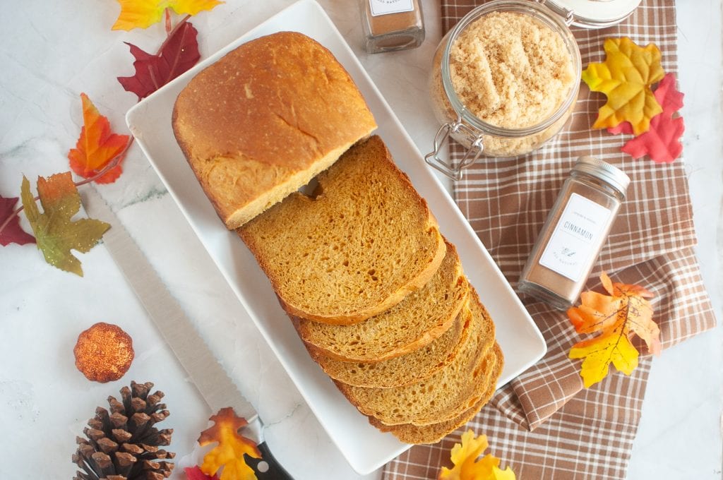 Pumpkin bread slices on white platter with fall leaves and spices, autumn baking, cozy seasonal food, vegan pumpkin bread recipe, Veggie Fun Kitchen.