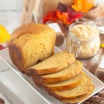 Pumpkin bread slices on white platter with fall leaves and spices, autumn baking, cozy seasonal food, vegan pumpkin bread recipe, Veggie Fun Kitchen.