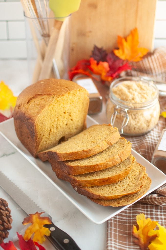 Pumpkin bread slices on white platter with fall leaves and spices, autumn baking, cozy seasonal food, vegan pumpkin bread recipe, Veggie Fun Kitchen.
