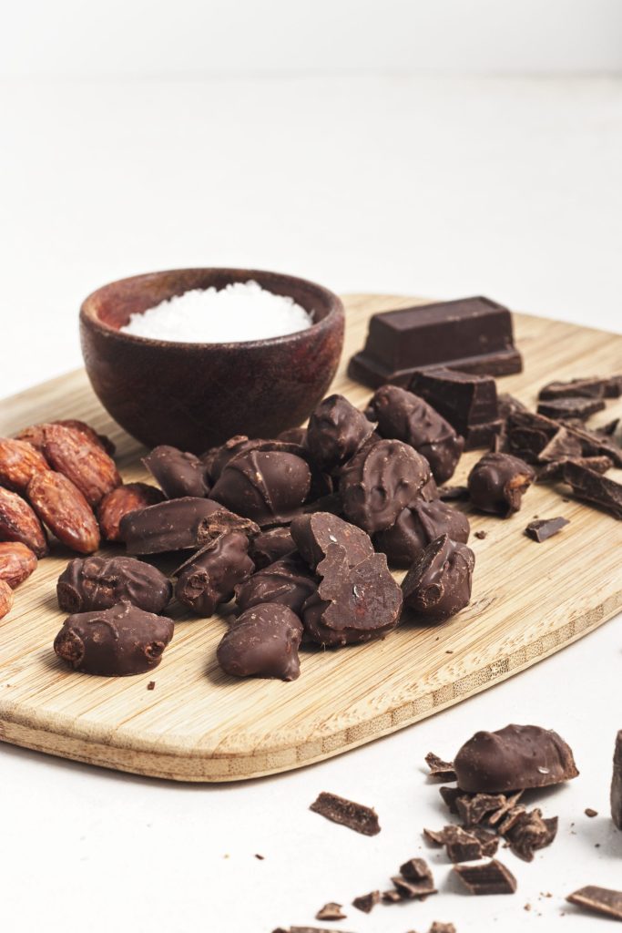 Chocolate almonds, coconut flakes, and chopped dark chocolate on wooden board for vegan baking.