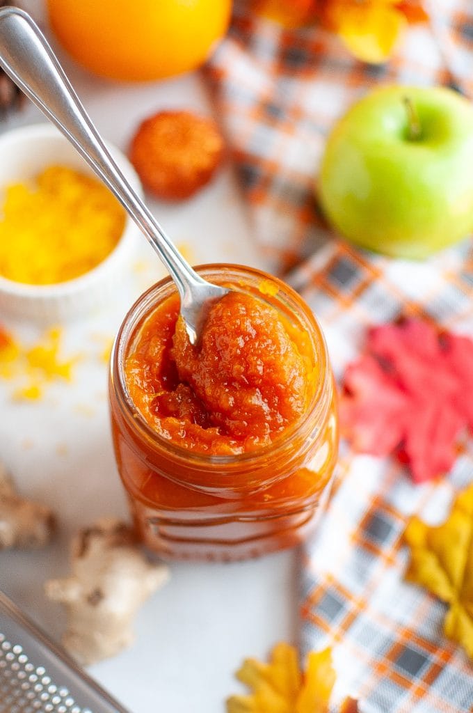 Spoon dipped in Jar of pumpkin jam surrounded by fall decor.