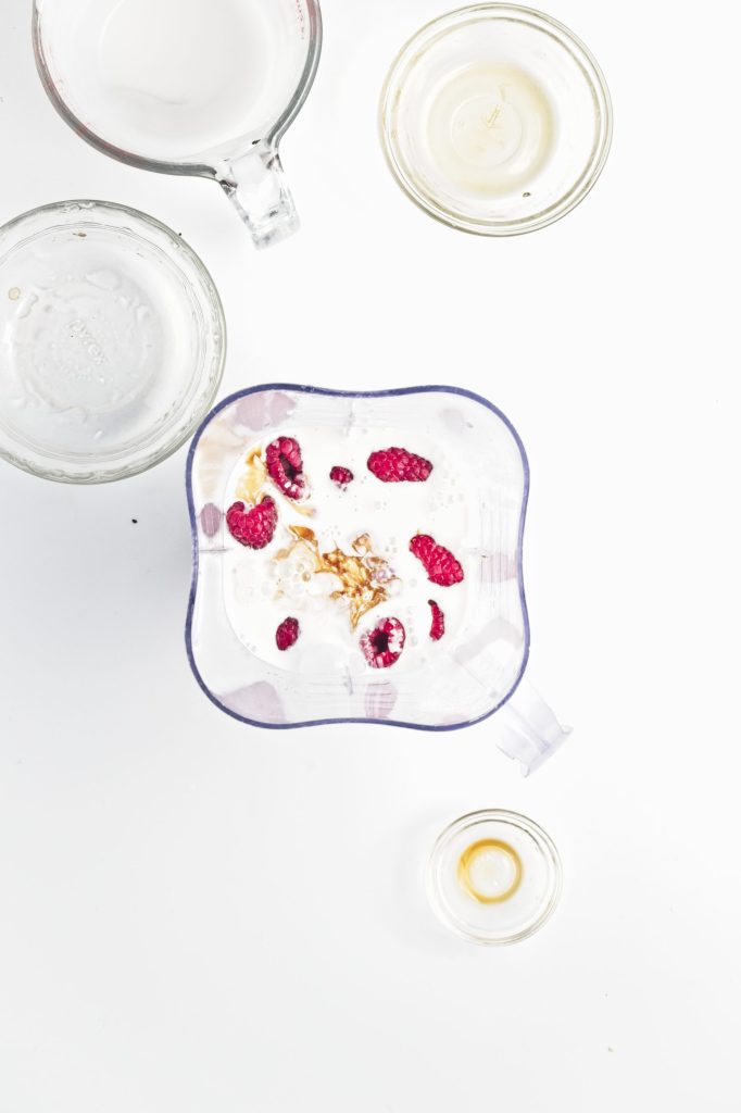 ingredients in the blender.You can see the raspberries on top waiting to be blended with the coconut milk and other ingredients. Three cups surround the the blender