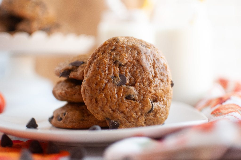 A stack of four pumpkin cookies with one fallen off the stack.
