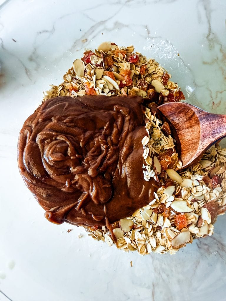 adding the melted heated almond butter mixture to the oat, nut and fruit mixture
