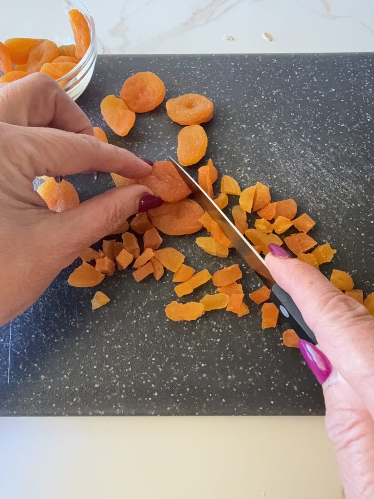 Dried apricots being chopped on a black cutting board for almond butter oat bars