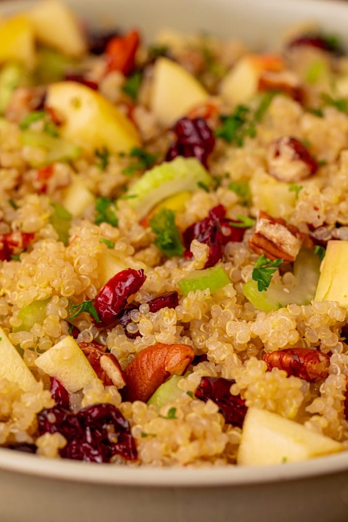 A close-up of a quinoa salad with chopped apples, celery, dried cranberries, pecans, and fresh parsley, all mixed together in a bowl.