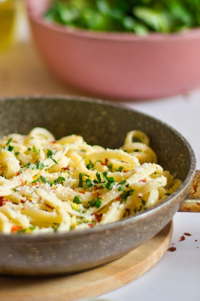 Creamy veggie pasta with fresh herbs in a skillet on a wooden board.