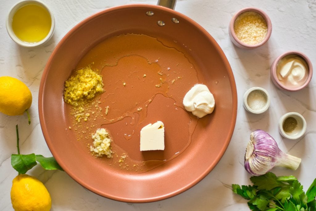 Fresh garlic, lemon, and herb ingredients on a marble surface for veggie recipes.