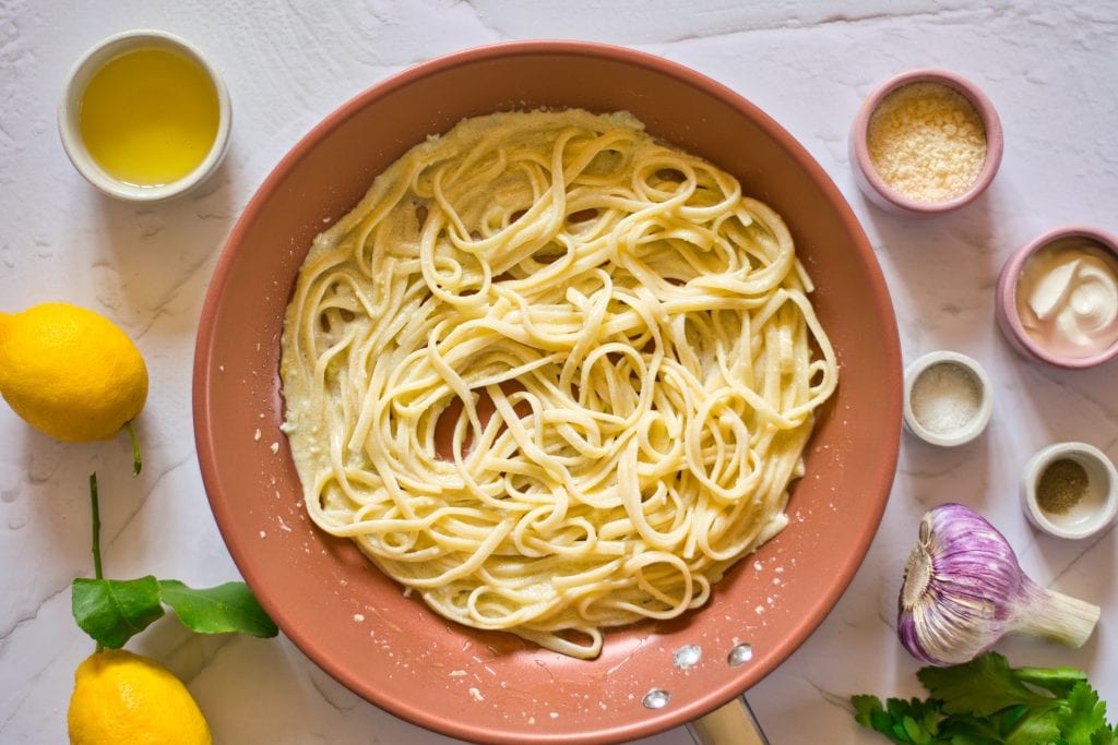 Creamy fettuccine pasta with garlic and lemon, surrounded by fresh ingredients and seasonings for vegan recipes.
