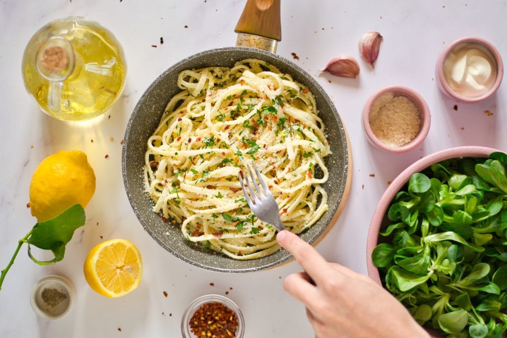 creamy vegan pasta with fresh herbs, lemon, garlic, and olive oil, surrounded by ingredients for vegan pasta dish.