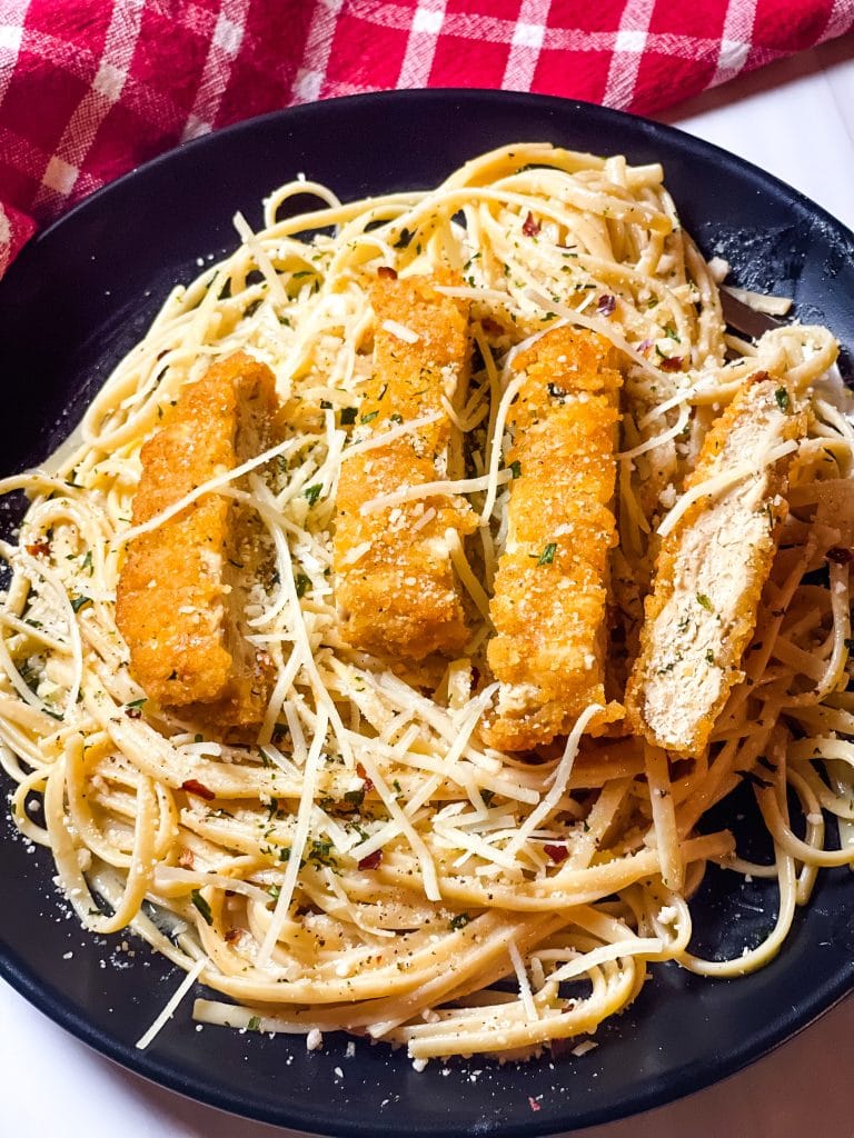 Golden vegan chicken tenders over creamy garlic parmesan pasta with shredded cheese and herbs.
