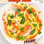 A bowl of colorful Thai-inspired mango salad with red bell peppers, onions, fresh herbs, green onions, and peanuts. The text reads Thai-Inspired Mango Salad and Vegan! on a white background.